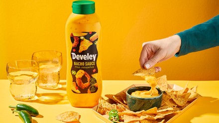 Develey Eine Hand dippt mit einem Nacho in die Nacho Sauce