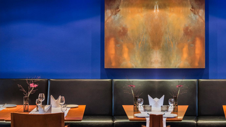 Tische des Gourmetrestaurant M im Mintrops Stadt Hotel in Essen vor einer blauen Wand mit goldenem Gemälde