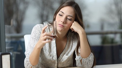 Gelangweilte Frau in einem Lokal blickt auf ein leeres Glas