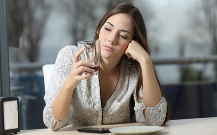 Gelangweilte Frau in einem Lokal blickt auf ein leeres Glas