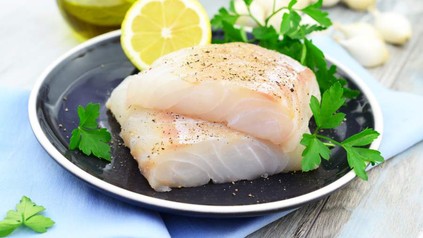 Eine Portion Fisch auf einem Teller mit Zitrone und Petersilie angerichtet