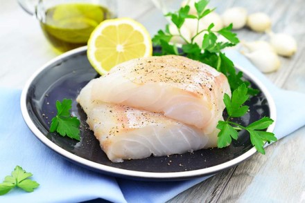 Eine Portion Fisch auf einem Teller mit Zitrone und Petersilie angerichtet