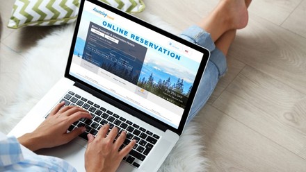 Eine Frau sitzt auf dem Boden und tippt auf einem Laptop auf dem eine Hotelbuchungswebseite geöffnet ist