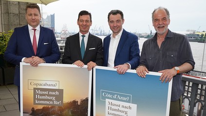 v.r.: Schauspieler Marek Erhardt, Dirk Kowalke, Gastronom und Inhaber Fischereihafen Restaurant, Ingo Peters, General Manager Fairmont Hotel Vier Jahreszeiten Hamburg, und André Vedovelli, Vorstand Elysée-Hotel AG, halten Plakate mit der Aufschrift „Kannst in Hamburg bleiben für“ und „Musst nach Hamburg kommen für“ hoch.