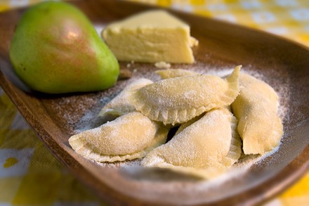 Mit Mehl bedeckte Ravioli, ein Stück Bergkäse und eine Birne auf einem Holzbrett