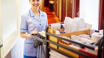 Ein lächelndes Zimmermädchen mit Wagen auf einem Hotelgang