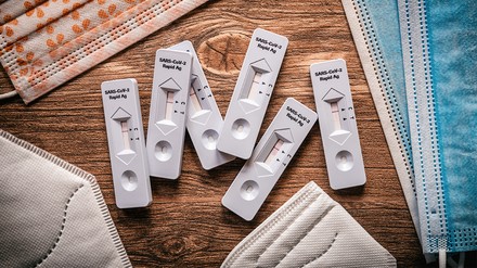 Corona-Schnelltests umringt von Masken liegen auf einem Tisch