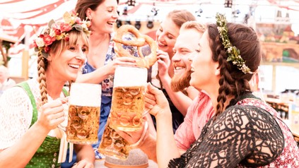 Gruppe von Freunden am Biertisch stoßen mit Maß an und lachen auf dem Oktoberfest.