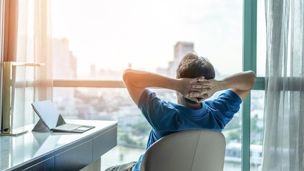 Junger Mann sitzt zum Arbeiten im Hotelzimmer und genießt den Ausblick