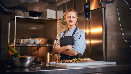 Junge Köchin steht selbstbewusst in der Küche