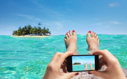 FRau liegt im Wasser und fotografiert eine Insel mit dem Handy
