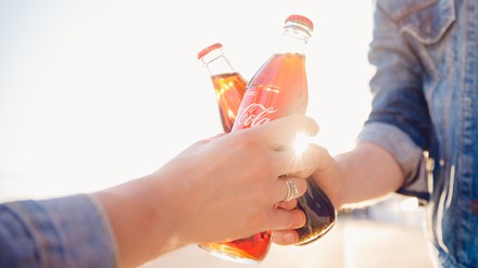 Zwei Personen stoßen mit Coca Cola an