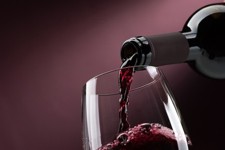 Mit einer Weinflasche wird ein Glas Wein eingeschenkt