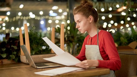 Junge Gastronomie mit Papieren vor dem Laptop