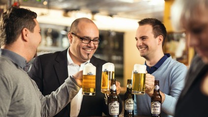 Drei Männer stoßen in Bar mit Bier an