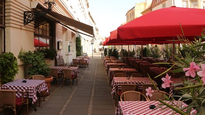 Gehsteig vor Restaurant mit vielen Tischen und Sonnenschirmen