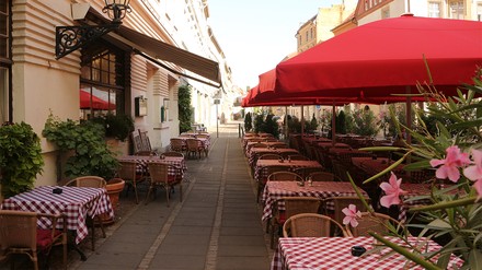 Gehsteig vor Restaurant mit vielen Tischen und Sonnenschirmen
