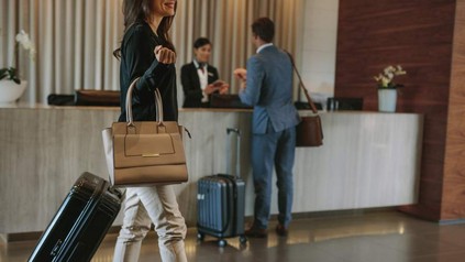 Eine Hotellobby, in der ein Geschäftsmann seinen Schlüssel entgegennimmt und eine Geschäftsfrau zur Rezeption geht