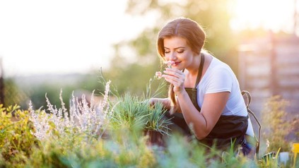 Frau in Garten riecht an Blume