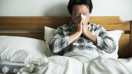 Mann liegt erkältet im Bett