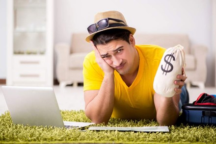 Mann mit Geldsack in der Hand sitzt verzweifelt vor Laptop