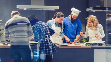 Koch und Teilnehmer eines Kochkursen um die Kücheninsel versammelt