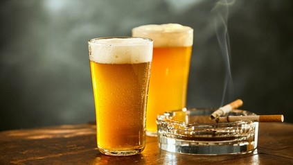 Zwei rauchende Zigaretten in einem Aschenbecher neben dem zwei Gläser Bier stehen