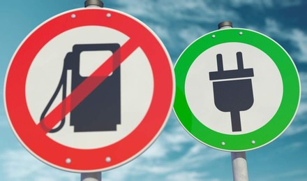 Zwei Straßenschilder: eines zeigt ein durchgestrichenes Tanksymbol, das andere einen grünen Elektrostecker