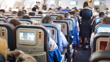 Ein vollbesetztes Flugzeug in dem Flugbegleiter gerade mit dem Servieren von Getränken beschäftigt sind