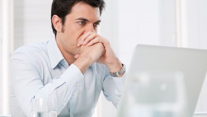 Ratloser Mann sitzt vor Laptop