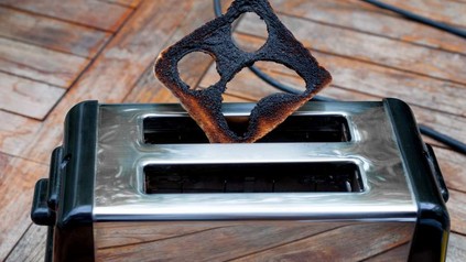 Ein Toast aus dem ein erschrockenes Gesicht geschnitten wurde steckt verbrannt auf einem Toaster