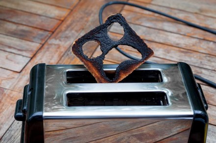Ein Toast aus dem ein erschrockenes Gesicht geschnitten wurde steckt verbrannt auf einem Toaster