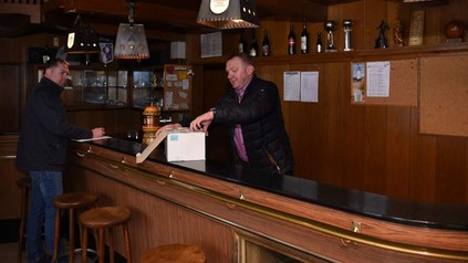 Zwei Männer stehen in hinter einer leeren Bar und öffnen einen Karton
