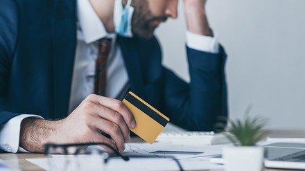 Unglücklicher Geschäftsmann, der seine Kreditkarte hält, seine Augen geschlossen hat und seinen Kopf auf seiner Hand aufstützt