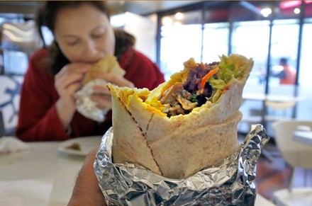 Ein Mann hält einen angebissenen Döner während eine Frau ihm gegenüber ebenfalls in einen Döner beißt