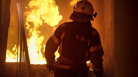 Ein Feuerwehrmann steht in voller Montur vor einem Feuer in einem Gebäude