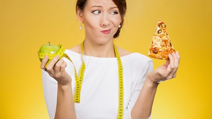 Frau misst Apfel mit Maßband und sieht auf ein Stück Pizza