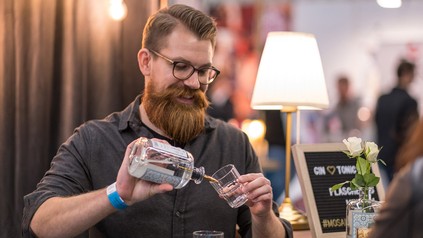 Ein Bartender gießt Gin aus der Flasche in ein dazu passendes Glas.