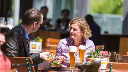 Mann und Frau sitzen beim Essen und einem Bier in einem Gastgarten.