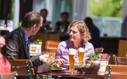 Mann und Frau sitzen beim Essen und einem Bier in einem Gastgarten.