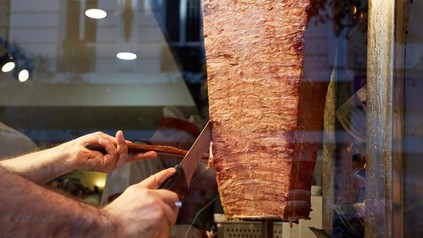 Ein Mitarbeiter eines Döner Imbisses schneidet Fleisch von einem Dönerspieß
