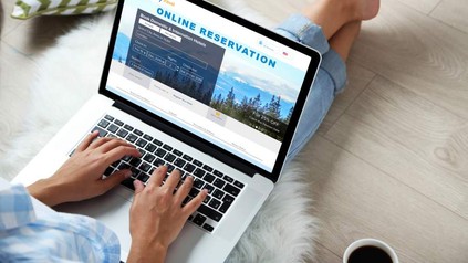 Eine Frau sitzt auf dem Boden und tippt auf einem Laptop auf dem eine Webseite für Onlinereservierungen geöffnet ist