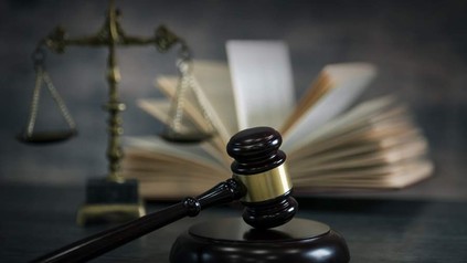 Ein Richterhammer liegt vor einem offenen Buch und einer Waagschale