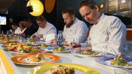 Mehrere Köche probieren verschiedene Speisen und machen sich Notizen für die Bewertung