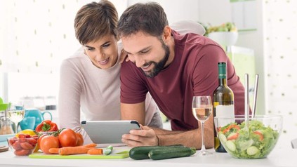 Ein Pärchen beim Kochen blickt auf ein Tablet