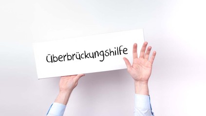 Hände halten Schild mit der Aufschrift "Überbrückungshilfe" in die Luft
