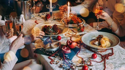 Ein weihnachtlich gedeckter Tisch an dem mehrere Personen gutes Essen verzehren und mit Sekt anstoßen
