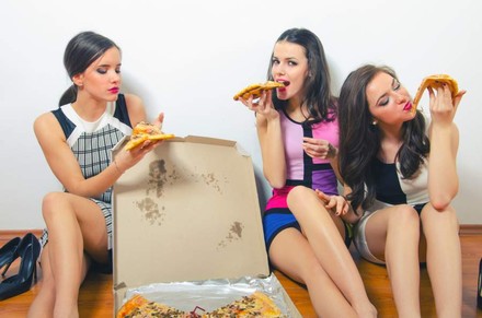 drei Frauen sitzen um einen Pizzakarton herum und essen Pizza