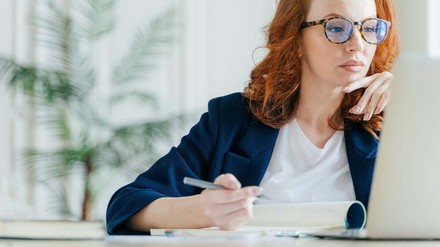 Junge Frau sitzt vor dem Laptop und macht sich Notizen zum Webinar