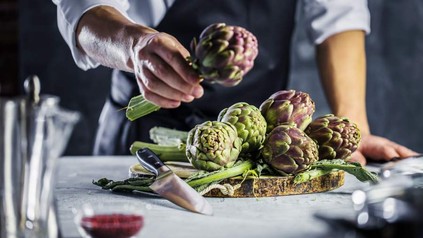 Ein Koch steht vor einem Holzbrett mit einigen Artischocken darauf